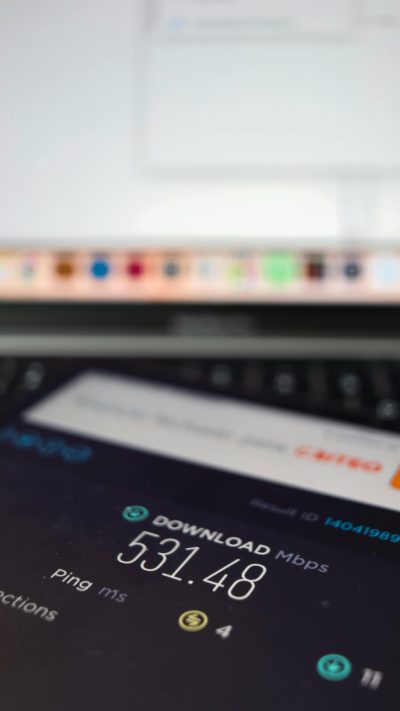 pexels-photo-14690386-14690386 Close-up of a smartphone showing internet speed test results with a laptop in the background.